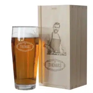 Idée cadeau noel originale pour homme : verre à bière personnalisé Amikado avec photo imprimée, posé sur une table en bois avec mousse dorée, ambiance conviviale et joyeuse, cadeau humoristique et tendre à offrir à un amateur de bière ou à un ami proche.