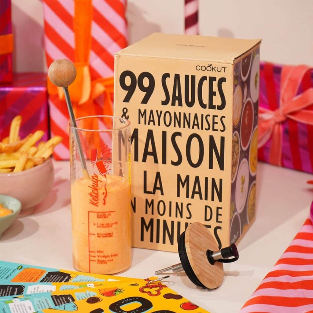 Idée cadeau anniversaire DIY pour sa femme, son mari ou un ami fan de cuisine : kit Les Raffineurs 99 sauces comprenant livre de recettes, ustensiles et ingrédients de base, posé sur une table en bois avec bols remplis d’assaisonnements colorés, ambiance conviviale et gourmande, mettant en valeur l’esprit fait main et le plaisir de cuisiner maison.