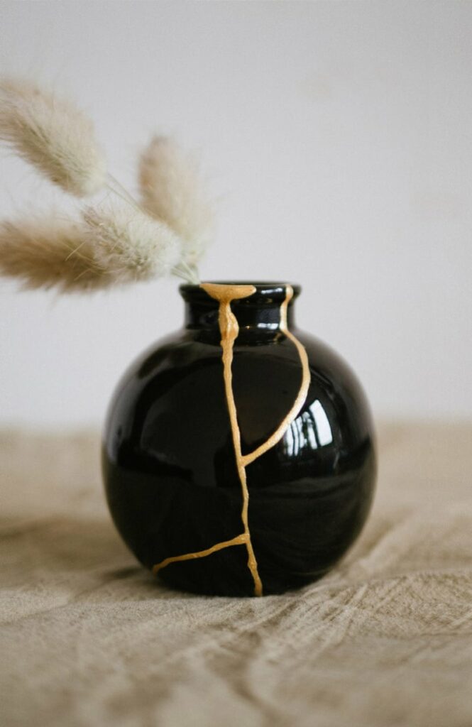 Idée cadeau d’anniversaire créatif : kit Kintsugi Les Raffineurs permettant de réparer une céramique avec de la poudre dorée, bol brisé, pinceau et colle posés sur une table en bois clair, lumière douce, ambiance apaisante et artisanale, évoquant l’art japonais de la réparation dorée et la beauté des imperfections.