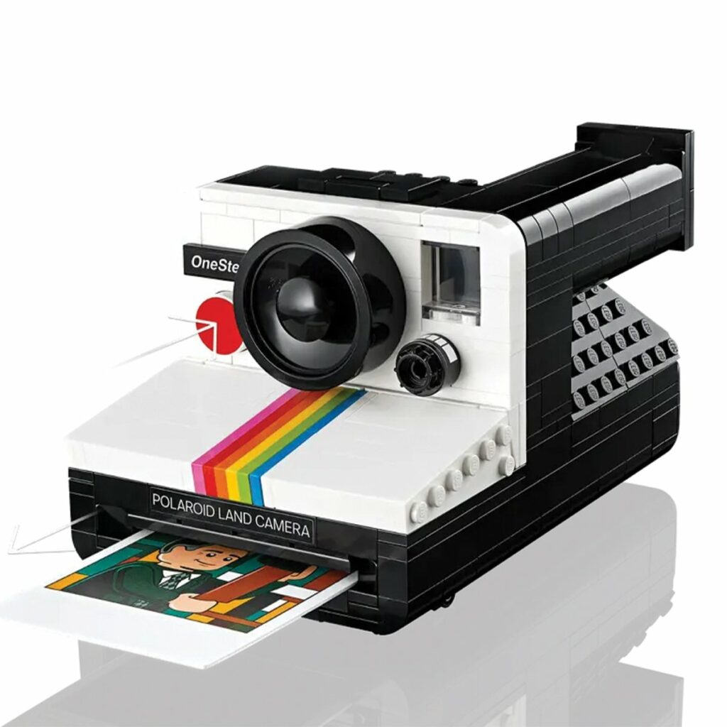 Idée cadeau anniversaire DIY pour sa femme, son mari ou un proche créatif : kit LEGO Polaroid Les Raffineurs avec briques colorées et manuel de montage, posé sur une table en bois clair avec l’appareil en cours d’assemblage, ambiance conviviale et ludique, mettant en valeur l’esprit fait main, la nostalgie photo et le plaisir de construire soi-même.