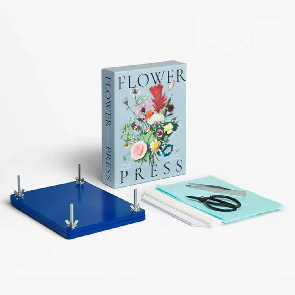 Idée cadeau anniversaire DIY pour sa femme, sa sœur ou son amie créative : presse à fleurs Les Raffineurs en bois avec vis métalliques, posée sur une table claire entourée de fleurs séchées colorées, ambiance naturelle et douce, mettant en valeur l’esprit artisanal, la création fait main et la poésie des souvenirs préservés.