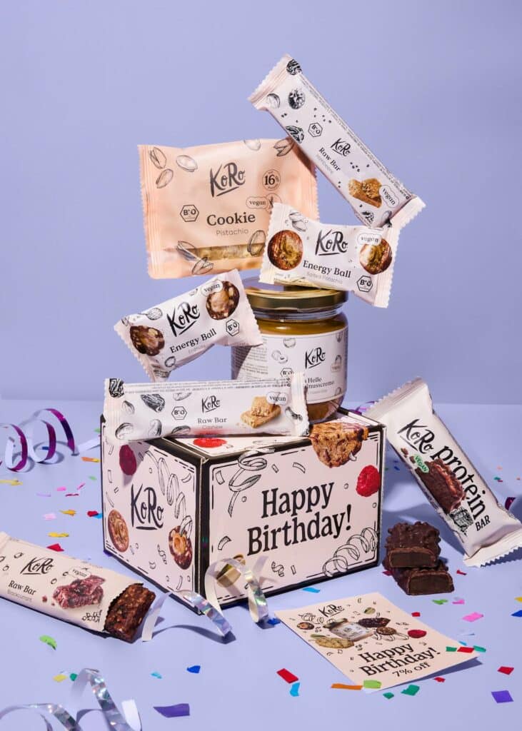 Coffret découverte de snacks KoRo déballé sur un lit, idée cadeau gourmande pour une soirée pyjama d'ados