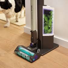 Aspirateur sans fil Shark PowerDetect Clean & Empty IP3251EUT photographié sur un parquet clair, mis en situation dans un salon, montrant son design moderne, sa technologie d’aspiration intelligente avec vidage hygiénique automatique, et ses performances idéales pour les grandes surfaces et les sols variés dans un usage domestique intensif.