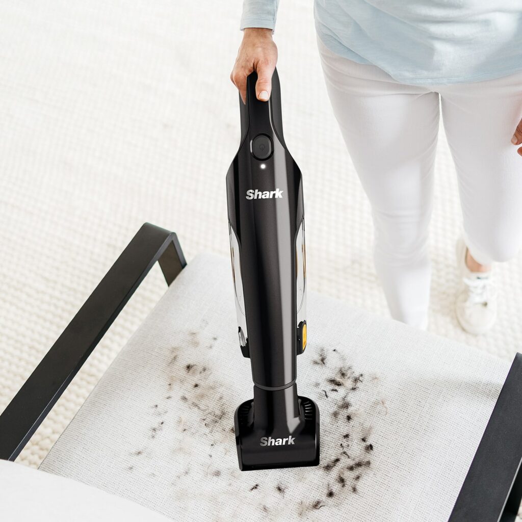 Aspirateur à main Shark CH950EUT en train de nettoyer un canapé plein de poils de chat, démontrant sa brosse motorisée spéciale animaux, sa prise en main facile et sa puissance adaptée aux petites surfaces, voitures, tissus et coins difficiles d’accès.