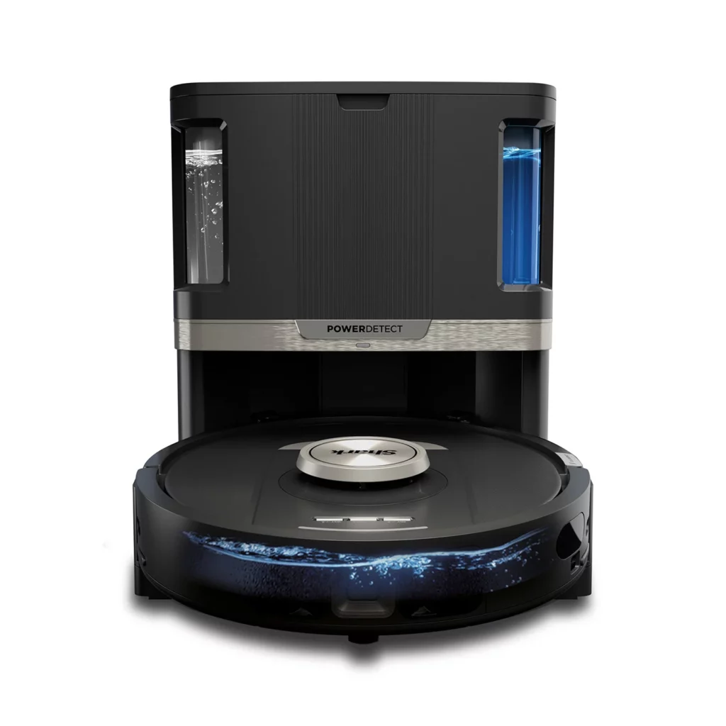 Robot aspirateur et laveur Shark PowerDetect NeverTouch RV2800ZEEUWH photographié dans un appartement moderne, en train de se vider automatiquement dans sa station d’accueil, illustrant ses fonctions auto-nettoyantes, auto-remplissantes et son pilotage intelligent via appli mobile pour une autonomie totale dans l’entretien de la maison.