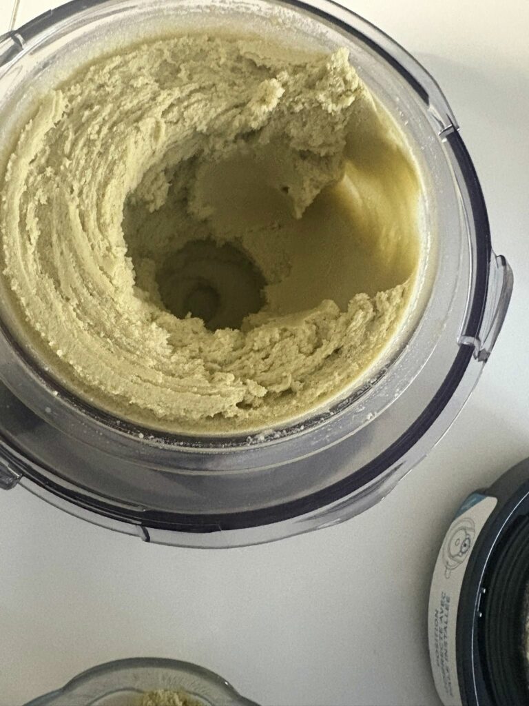 Glace vegan maison à la pistache préparée au Ninja Creami Deluxe, réalisée sans produits laitiers, avec lait de coco, lait végétal et purée de pistache, servie avec topping crème de pistache pour un goût intense, dessert végétal crémeux, peu sucré, adapté aux intolérants au lactose et à la caséine, recette saine et gourmande à la fois, photographiée dans un bac prêt à mixer