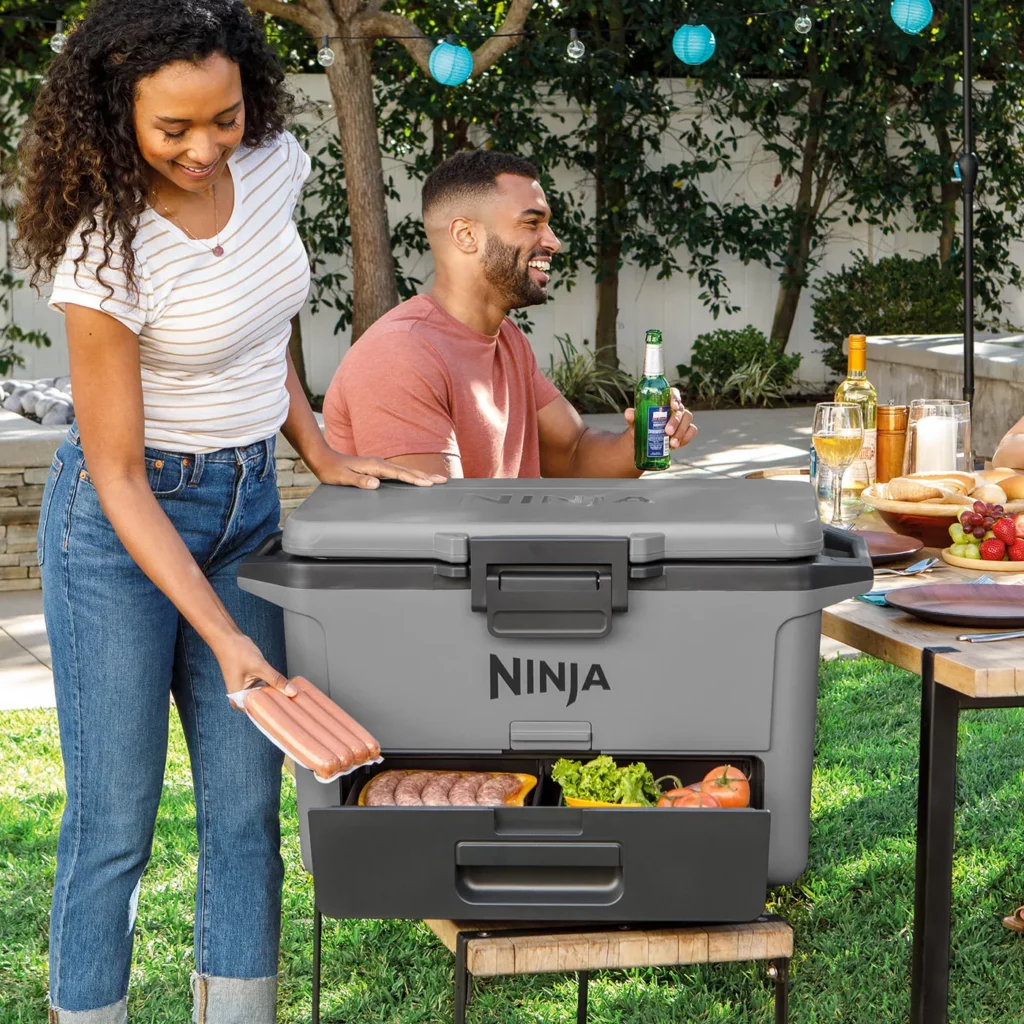 Vue de la glacière Ninja FrostVault 47 L ouverte, avec son tiroir Dry Zone visible et des boissons à l’intérieur – design robuste et moderne, idéale pour conserver des aliments et boissons au frais plusieurs jours lors de pique-niques ou sorties camping.
