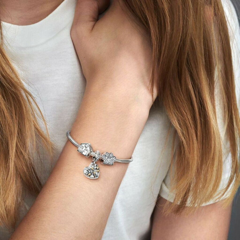  Zoom sur un bracelet Pandora en argent avec plusieurs charms dont un cœur, une étoile et une perle nacrée, soulignant la variété de bijoux proposés par Pandora : bracelets, bagues, colliers, charms, tous personnalisables et pensés comme des souvenirs à porter au quotidien.
