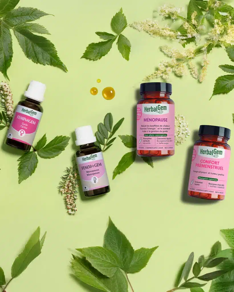 Flacons Herbalgem alignés sur un plan en bois, accompagnés de rameaux de bourgeons frais, mettant en valeur la gemmothérapie artisanale et le respect du vivant propre à la marque.