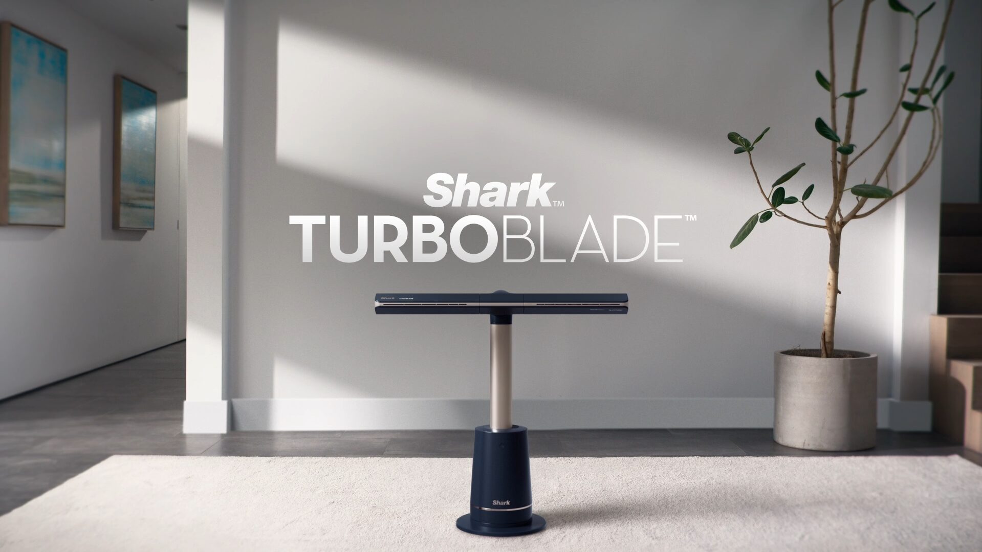Photographie du ventilateur Shark TurboBlade, un modèle sans pales à haute vitesse, élégant et moderne, posé dans un salon contemporain, illustrant parfaitement le design épuré de ce ventilateur Shark. Ce visuel met en valeur les dimensions élancées de la version XL du Shark TurboBlade fan, apprécié pour sa puissance, son fonctionnement silencieux et sa diffusion d'air uniforme. Idéal pour illustrer un avis sur le Shark TurboBlade, ce visuel rappelle aussi qu’il est disponible en France, notamment chez Boulanger, Costco ou sur le site officiel de Shark Europe. On aperçoit à l’arrière une télécommande, rappelant les fonctionnalités pratiques du ventilateur Shark TurboBlade France, parfait pour ceux qui recherchent une alternative esthétique et efficace aux ventilateurs traditionnels.