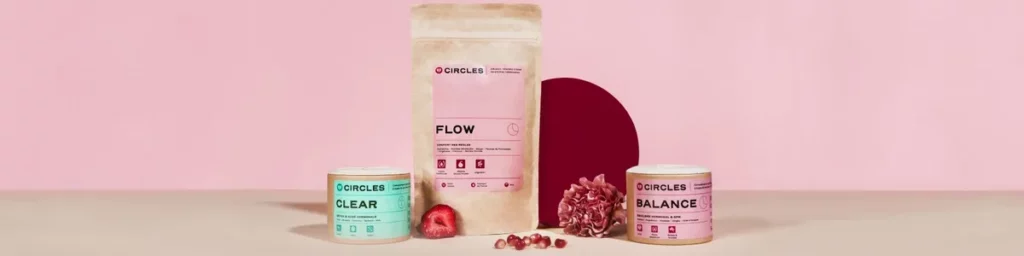 photo d’ambiance lifestyle d’une main féminine tenant un flacon Circles sur une table en bois clair, entourée de plantes et d’un carnet ouvert, représentant une routine bien-être naturelle et féminine