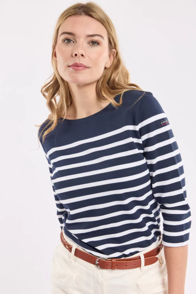 Une élégante marinière Armor Lux aux rayures bleu marine et blanches, pliée soigneusement dans un papier de soie, prête à être offerte pour l’anniversaire d’une maman. Le logo brodé discrètement sur la manche rappelle la qualité artisanale de la marque bretonne. Cette image évoque un cadeau à la fois chic, durable et plein de tendresse, parfait pour célébrer une maman avec un vêtement qu’elle pourra porter longtemps, et associer à un joli souvenir d’anniversaire.