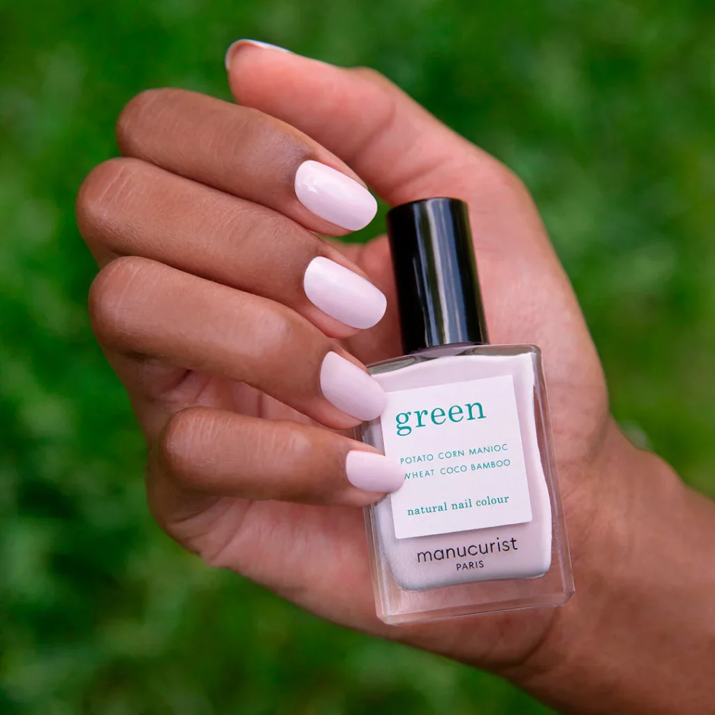 photo montrant une main en train d’appliquer un vernis green manucurist sur ongle court avec pinceau large et flacon visible, illustration de la pose facile à domicile