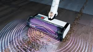 Aspirateur balai sans fil Shark Detect Clean en utilisation dans un salon avec tapis et parquet, montrant la détection automatique de la saleté et la polyvalence sur différents sols.