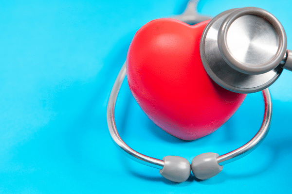 : Image d’un cœur rouge en 3D posé à côté d’une boîte de compléments alimentaires et de poissons gras, symbolisant la protection cardiovasculaire et la régulation du cholestérol