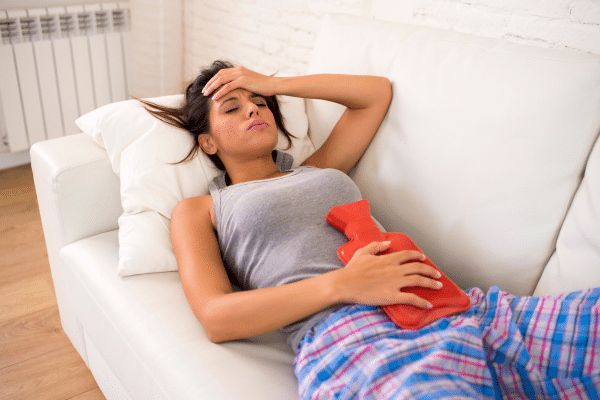Image d’une bouillotte chaude posée sur un lit avec une boîte de gélules naturelles à côté, représentant les compléments alimentaires pour soulager les règles douloureuses et le syndrome prémenstruel