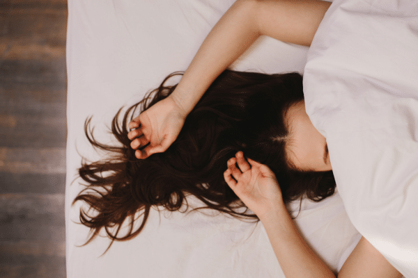 Image d’une femme qui dort paisiblement dans une chambre sombre et reposante avec une boîte de mélatonine sur la table de chevet, illustrant les compléments alimentaires pour favoriser un sommeil réparateur