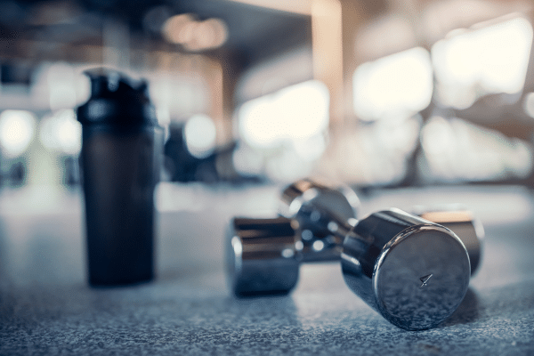Photo d’un sportif attachant ses baskets avec une gourde et des gélules naturelles posées à côté, illustrant les compléments alimentaires pour améliorer la performance et favoriser la récupération musculaire