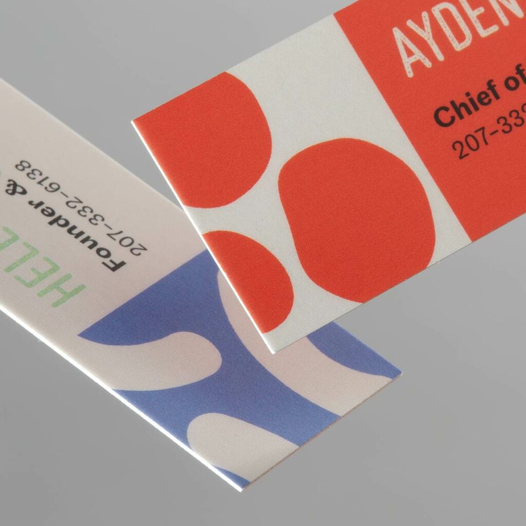 : Cartes de visite épaisses et design créées sur Moo, posées sur un bureau aux côtés d’un stylo et d’un carnet