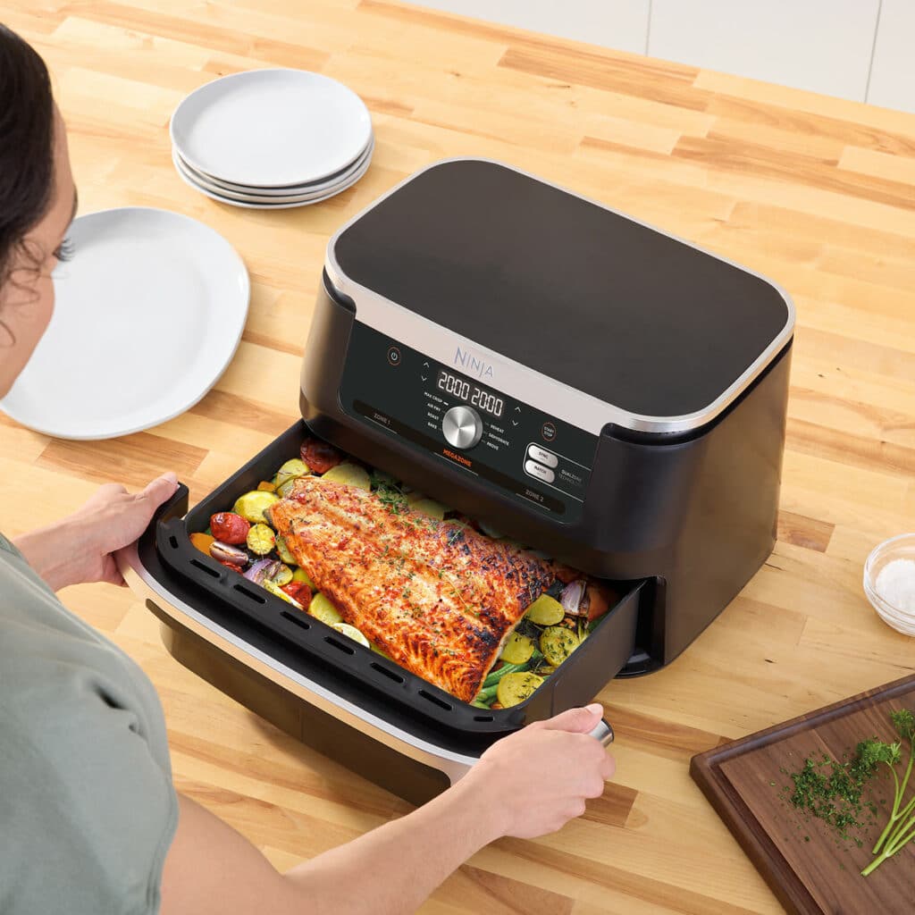 Photo montrant le tiroir du Ninja AF500EU divisé en deux zones indépendantes avec le séparateur, l’une remplie de frites croustillantes et l’autre de filets de saumon grillés, illustrant la technologie DualZone et la fonction MegaZone de 10,4 L.