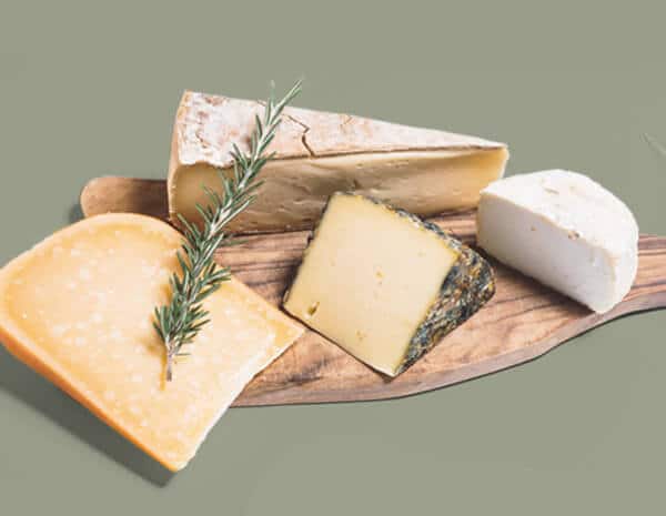 Idée cadeau d’anniversaire gourmande : coffret La Boîte du Fromager contenant quatre fromages artisanaux de saison, présentés sur une planche en bois avec pain et verre de vin, ambiance conviviale et chaleureuse, lumière dorée évoquant un apéritif entre amis ou en famille.