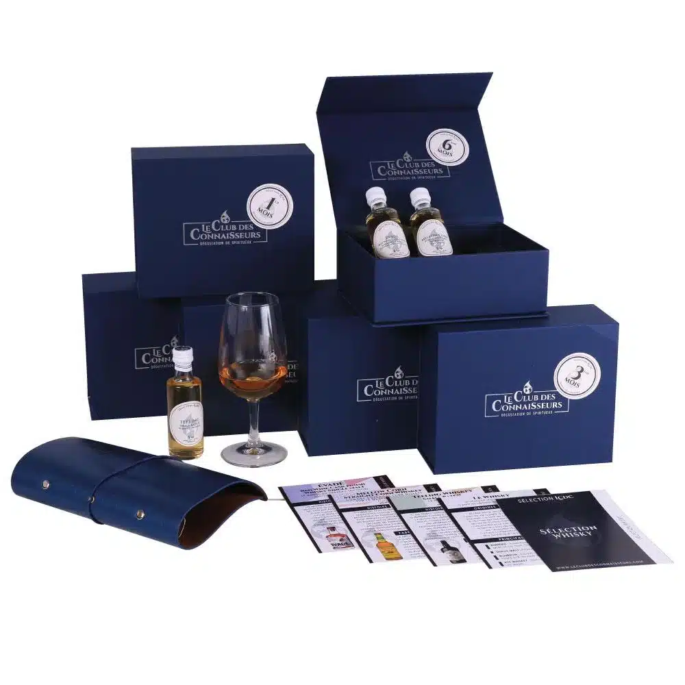 Idée cadeau anniversaire pour amateur de spiritueux : coffret Le Club des Connaisseurs contenant plusieurs fioles de dégustation de rhum, whisky ou gin premium, posées sur une table en bois avec verres à dégustation et livret explicatif, ambiance feutrée et chaleureuse, lumière dorée évoquant les reflets des alcools, parfait pour offrir à un homme, une femme ou un passionné d’expériences gustatives haut de gamme.