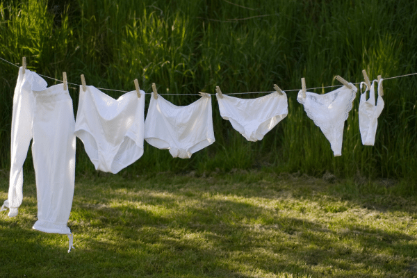 Photo de plusieurs culottes menstruelles en coton bio pliées sur une table en bois, illustrant un guide pratique sur le nombre de culottes nécessaires pour un cycle complet selon flux menstruel.