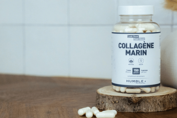 poudre de collagène marin dans une cuillère en bois posée sur un plan de travail avec smoothie en arrière-plan