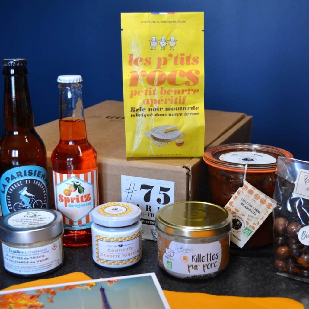 Idée cadeau anniversaire pour amateur de gastronomie française : coffret La Gourmet Box contenant produits du terroir, terrines, biscuits, confitures et bouteille de vin, présentés dans une boîte élégante sur une table en bois, ambiance chaleureuse et conviviale rappelant les saveurs régionales, parfait pour offrir à une femme, un homme ou un couple gourmand aimant les produits artisanaux.