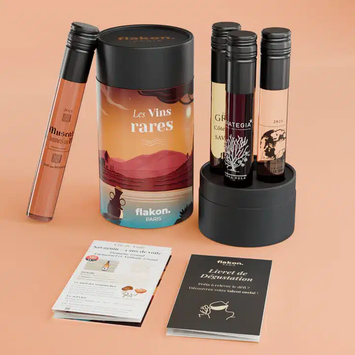 Idée cadeau anniversaire pour amateur de spiritueux : coffret Flakon contenant trois fioles de dégustation de rhum, whisky et gin premium, présentées dans un écrin noir élégant sur une table en bois clair, ambiance feutrée et raffinée, lumière dorée rappelant les reflets des alcools, cadeau idéal pour homme ou femme aimant la découverte et la dégustation sans abonnement.
