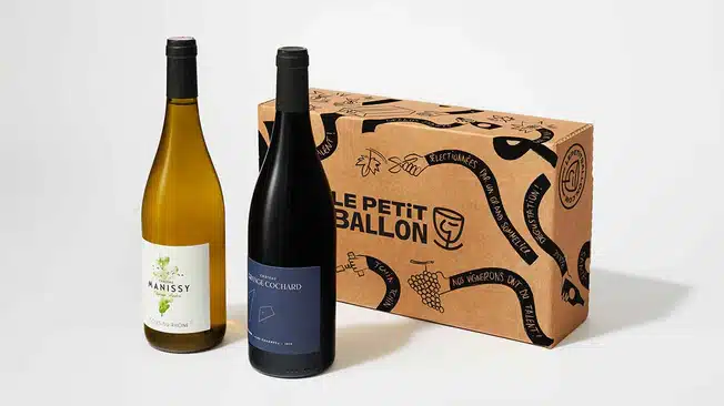 idée cadeau d’anniversaire pour amateur de vin : coffret Le Petit Ballon contenant deux bouteilles soigneusement choisies, verres à pied et fiches de dégustation sur une table en bois, ambiance conviviale et lumineuse, évoquant le plaisir d’une dégustation partagée à la maison.