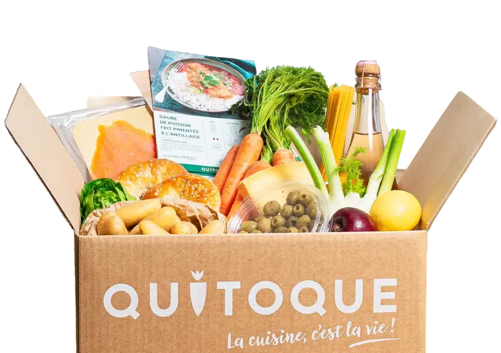 Idée cadeau anniversaire pour femme, homme ou famille : box Quitoque avec ingrédients frais et recettes à cuisiner livrés à domicile, présentés sur une table en bois avec légumes colorés, herbes aromatiques et fiches de préparation, ambiance conviviale et lumineuse, évoquant le plaisir de cuisiner maison et de partager un bon repas sans stress.