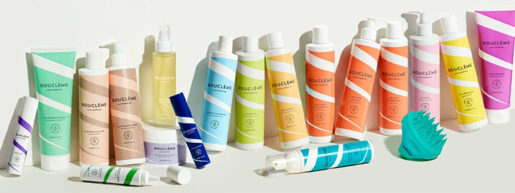 Portrait de la fondatrice Michele Scott-Lynch de Bouclème entourée de produits capillaires naturels, illustrant la philosophie clean et éthique de la marque britannique dédiée aux boucles.