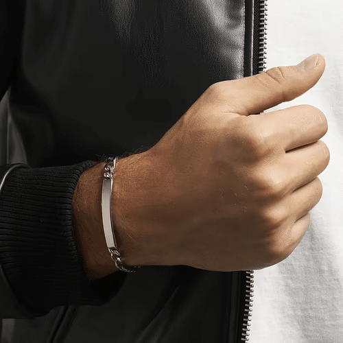 Bijoux homme Cléor, gourmette acier noir, bague acier brossé et collier pendentif ancre, posés sur un tissu sombre pour souligner la sobriété du design.