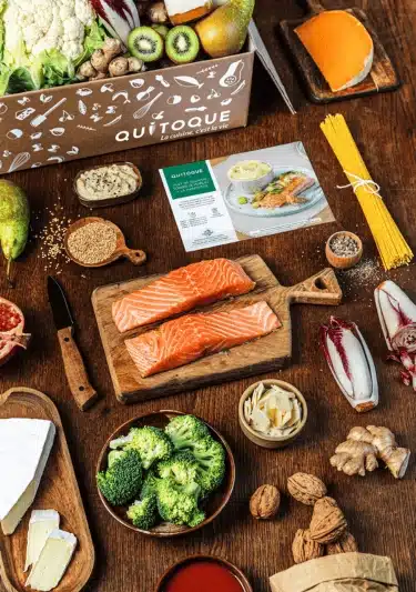 Femme souriante préparant un plat Quitoque dans une cuisine lumineuse. L’image illustre les avantages du service Quitoque (simplicité, gain de temps, qualité) et ses limites (prix, répétition de certaines recettes).