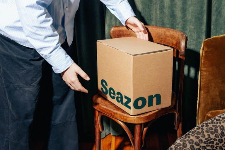 Photo d’une box Seazon France ouverte sur un plan de travail de cuisine avec plusieurs plats frais colorés, un logo Seazon bien visible et des étiquettes mentionnant les menus de la semaine. Image illustrant le concept de repas frais livrés à domicile et introduisant le test et avis Seazon.