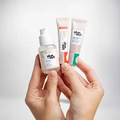 Portrait des fondatrices de Skin & Out avec flacons de soins et compléments alimentaires, représentant la philosophie in & out de la marque française dédiée aux peaux à imperfections.