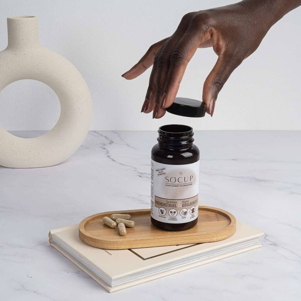 image du complément SPM de So Cup sur une table claire avec une infusion à côté, ambiance bien être et réconfort, mise en avant d’un soutien naturel pour les crampes et la fatigue menstruelle