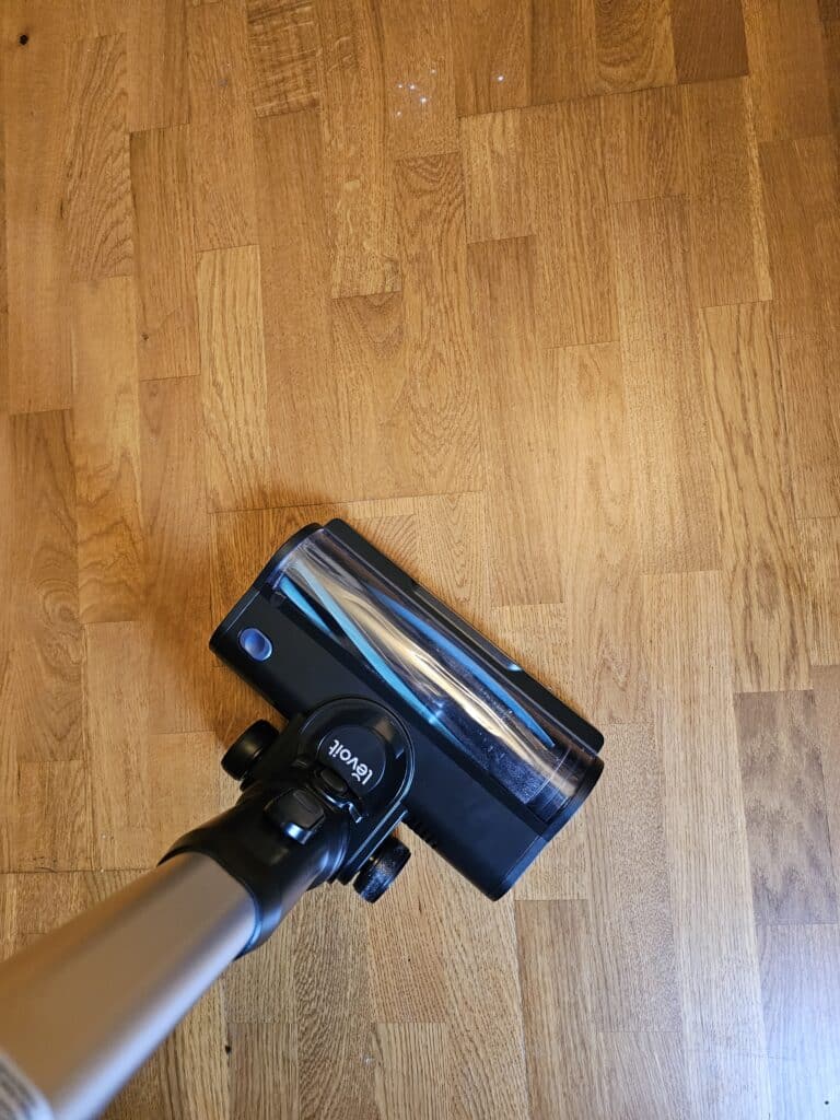 Aspirateur balai Levoit LVAC 300 passant sous un canapé et le long des meubles illustrant une bonne maniabilité un éclairage LED utile et un confort d’utilisation au quotidien