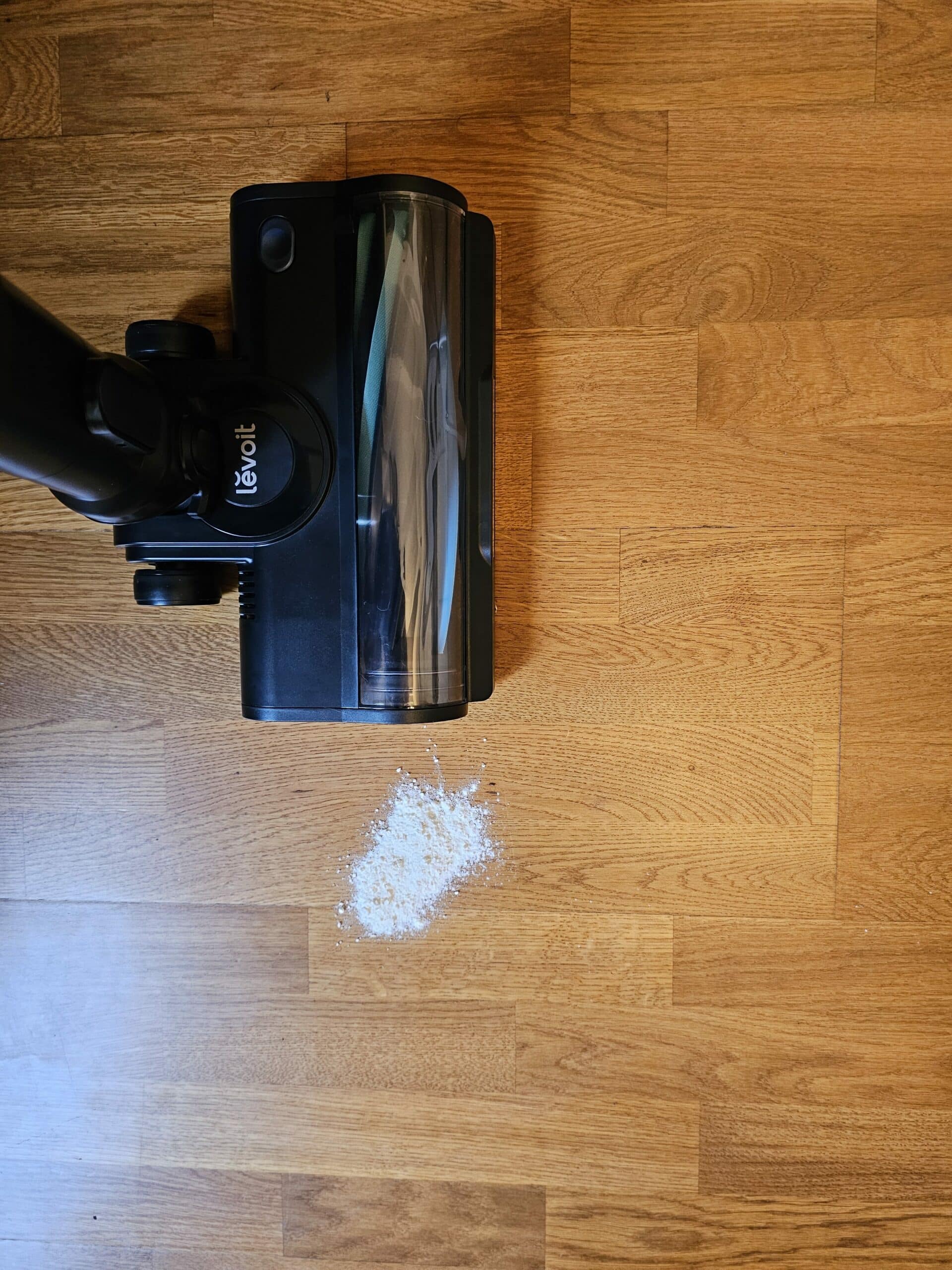 Aspirateur balai sans fil Levoit LVAC 300 aspirant des miettes et poussières fines sur un sol dur montrant une aspiration efficace en un seul passage dans un contexte réel