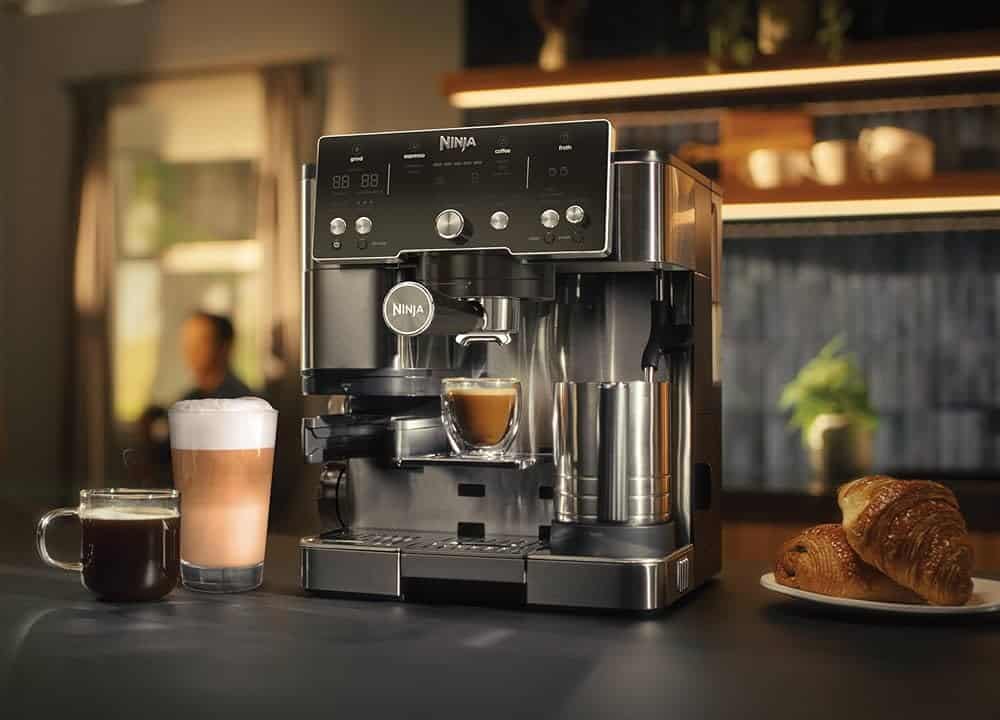 machine Ninja Luxe Café Essential ES501EU avec son moulin intégré, le porte filtre rempli de café fraîchement moulu et une tasse d’expresso double en sortie pour montrer le positionnement simple et efficace de cette machine expresso plus filtre destinée aux débutants barista.