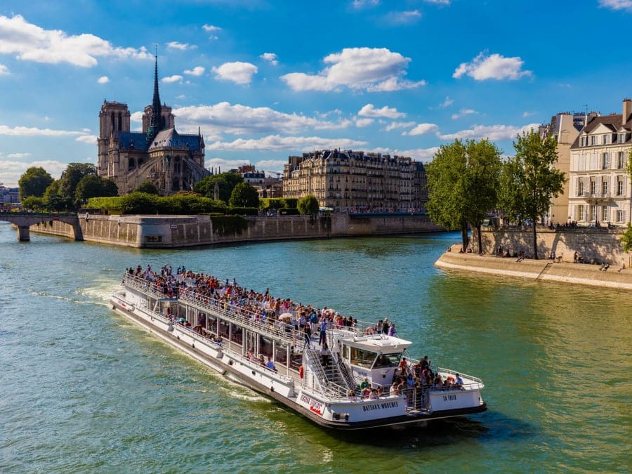 Bateau promenade sur la Seine passant sous un pont avec vue sur les monuments de Paris lors d’une croisière touristique
