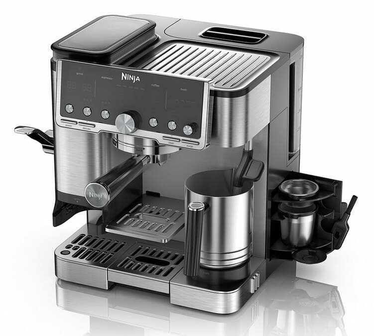 La Ninja Luxe Café Pro ES701EU vue de profil sur un plan de travail de cuisine, avec un espresso en train de couler dans une tasse en verre à double paroi posée sous le portafilter, la trémie à grains remplie visible en haut de la machine