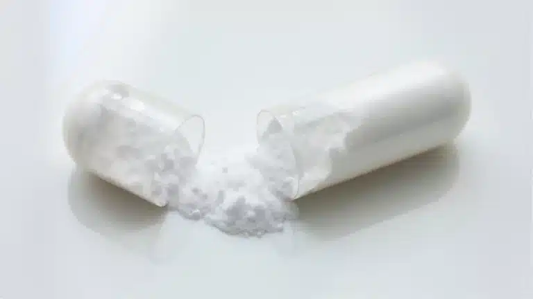le pilulier de gélules de magnésium bisglycinate Dynveo posé sur ma table de nuit, à côté d’un verre d’eau à moitié vide et de mon réveil affichant 22h40. C’est devenu mon rituel du soir depuis trois mois : deux gélules avalées avant de fermer les volets, jamais avec du café ni du thé pour ne pas gêner l’absorption. On distingue l’étiquette blanche avec la mention TRAACS et le nombre de gélules restantes visibles à travers le flacon transparent.