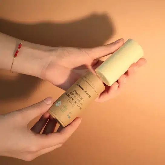 mes doigts qui poussent le carton du stick par le bas pour faire sortir le produit, photographié juste avant l’application matinale, la peau encore légèrement humide après la douche.
