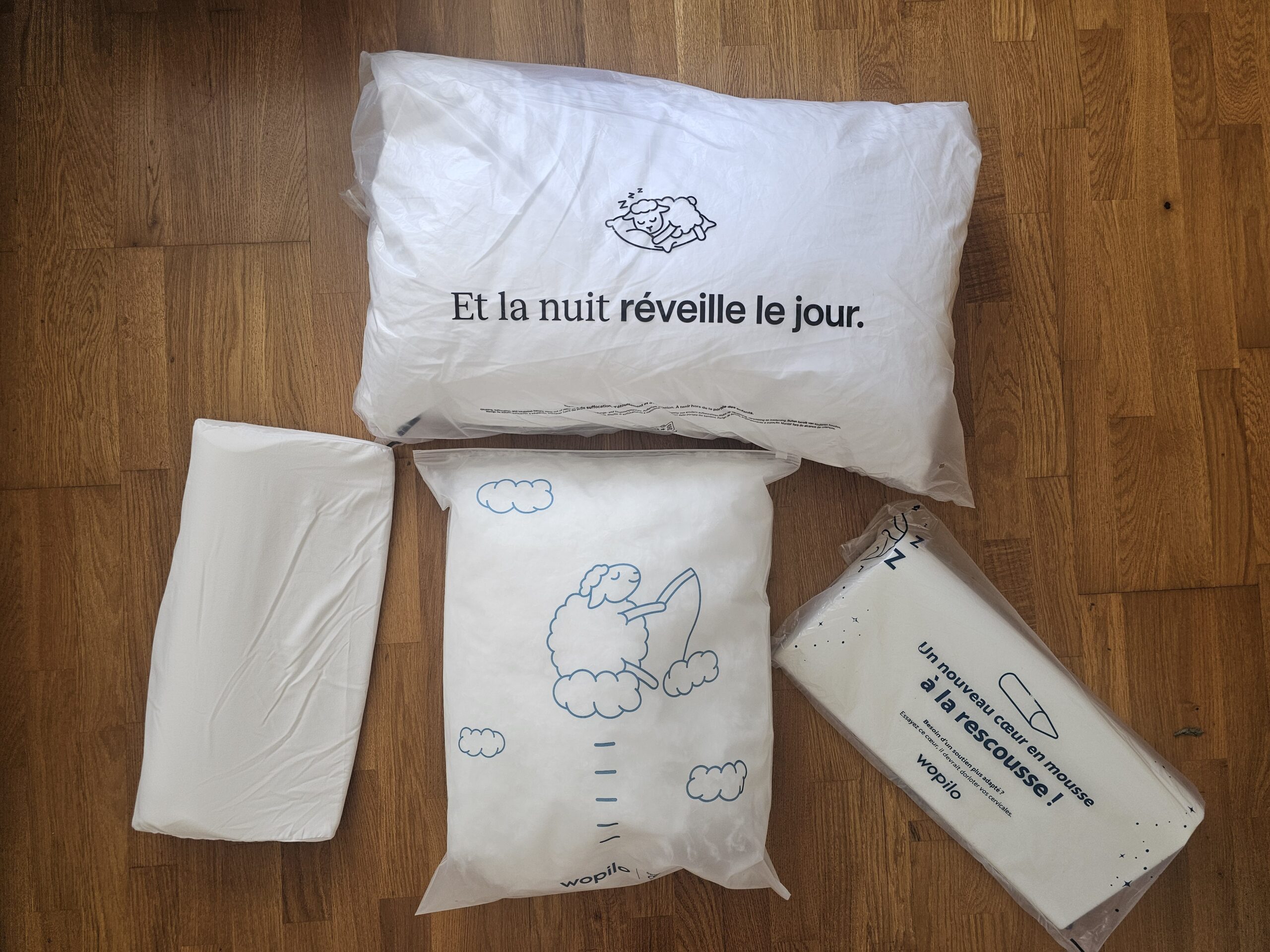 Contenu du carton wopilo plus étalé sur un lit : l'oreiller en housse percale blanche, les deux cœurs en mousse à mémoire de forme sortis de leur emballage, le sachet de microfibre supplémentaire et la carte du guide d'utilisation.